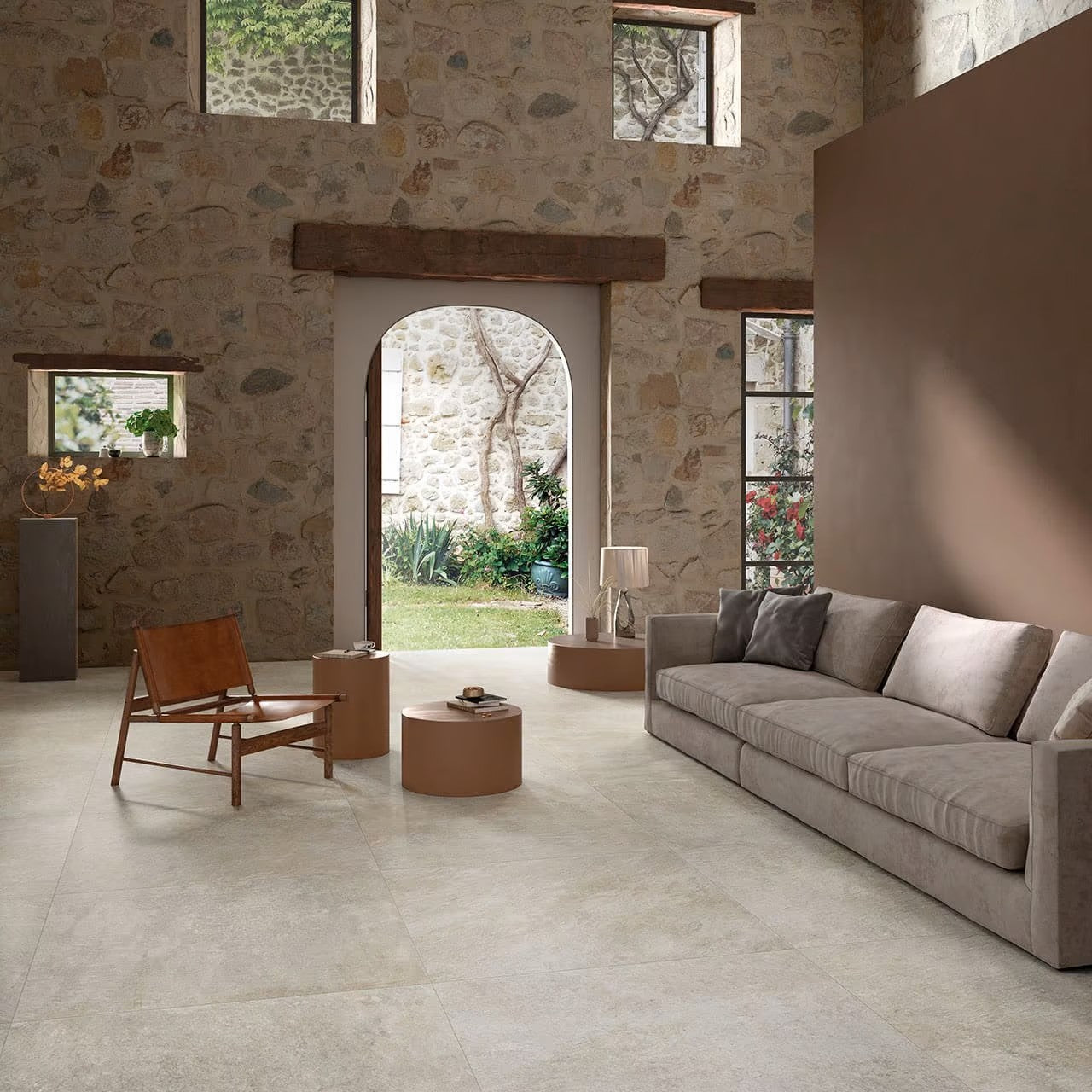 Absolute Moon 600x600mm light beige floor tiles installed in a rustic living room with exposed stone walls, a grey sofa, and leather accent chair.