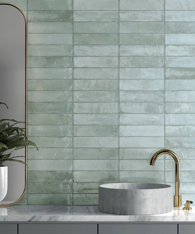 Acquarello Menta Glossy 60x246mm sage green rectangular tiles covering a full bathroom feature wall behind a concrete vessel sink, marble countertop, and brushed brass faucet.