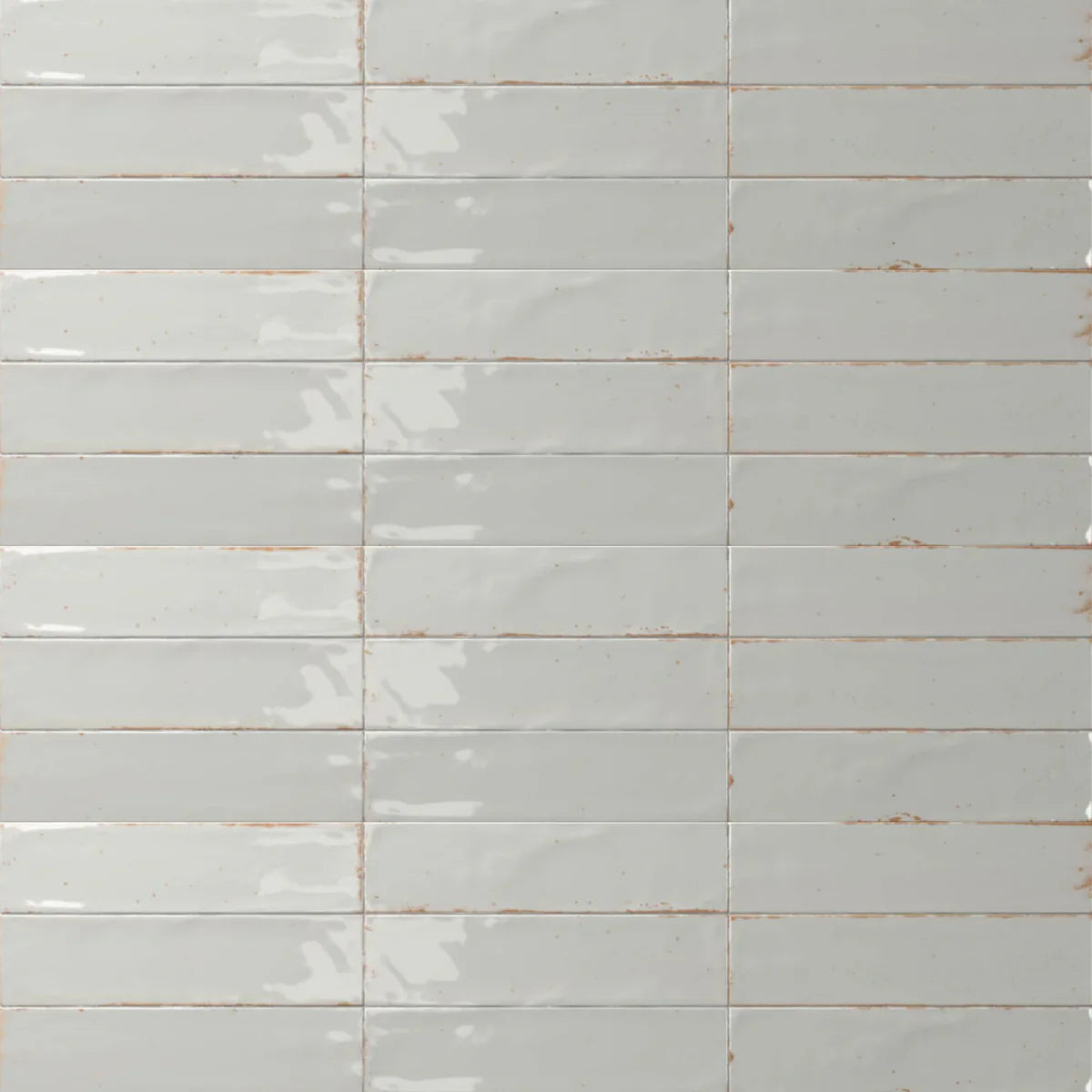 Close-up of Agadir Niebla 70x280mm glazed ceramic wall tiles in pale grey with a glossy finish and warm terracotta grout lines arranged in a stacked horizontal pattern.