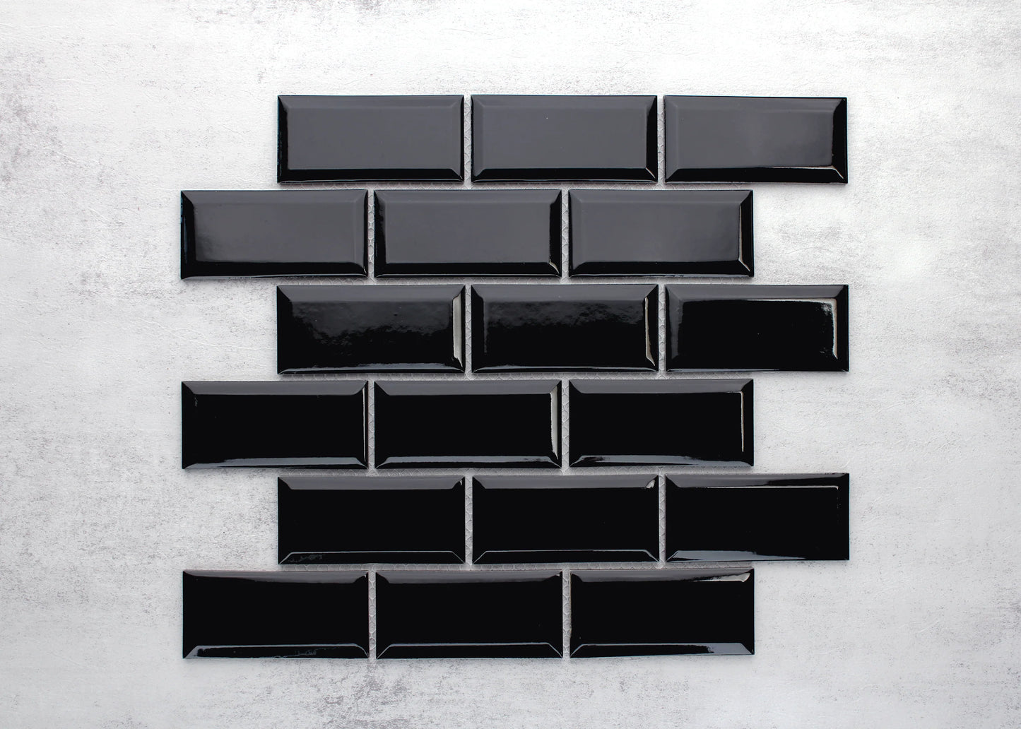 Black Gloss Glazed Porcelain Rectangle Bevelled Edge 45x95mm tiles arranged in a staggered brick-bond layout showing glossy finish and bevelled edges against a light concrete background.