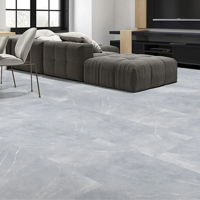 Bracca Light Grey Matt Rectified 600x600mm tiles installed as a large-format living room floor beneath a dark grey tufted sofa and ottoman.