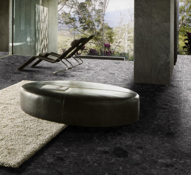 Breccia Dark Grey 600x600mm porcelain floor tiles installed in a contemporary open-plan living space with an oval leather ottoman, shag rug, and floor-to-ceiling glazing overlooking lush greenery.