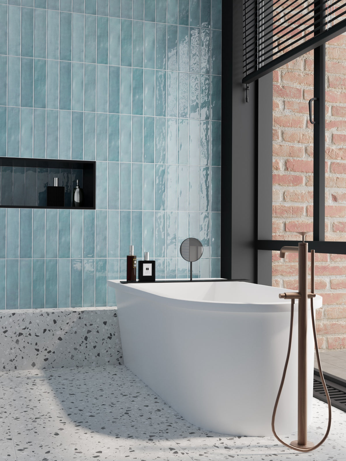 Caramela Sky Blue Gloss 75x300mm tiles installed vertically on a bathroom feature wall behind a white freestanding bath, paired with terrazzo flooring and exposed brick.