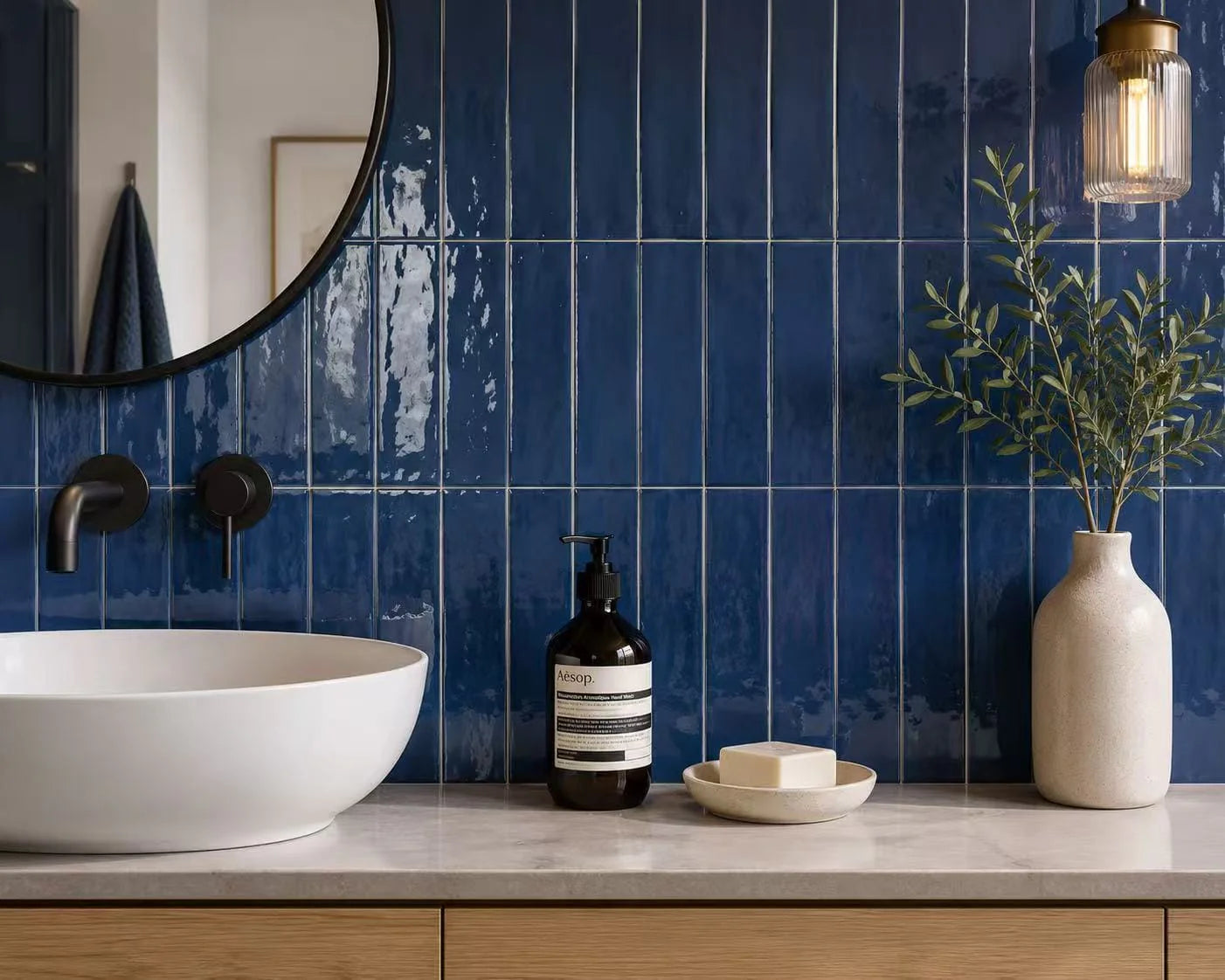 Casablanca Navy Blue Gloss 58x242mm tiles installed vertically as a bold bathroom feature wall behind a white vessel sink, marble countertop, and brass pendant light.
