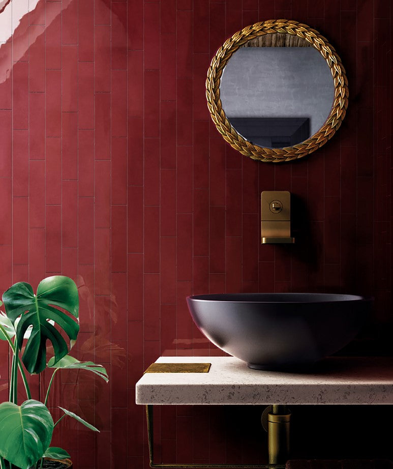 Casablanca Red Gloss 58x242mm tiles covering a dramatic bathroom feature wall, styled with a matte black vessel sink, gold leaf mirror, and monstera plant.