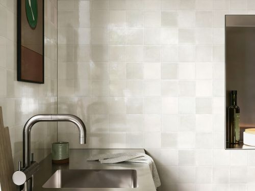 Chroma Dune Gloss 100x100mm white glossy square tiles installed on a bathroom wall behind a stainless steel sink and modern mixer tap.