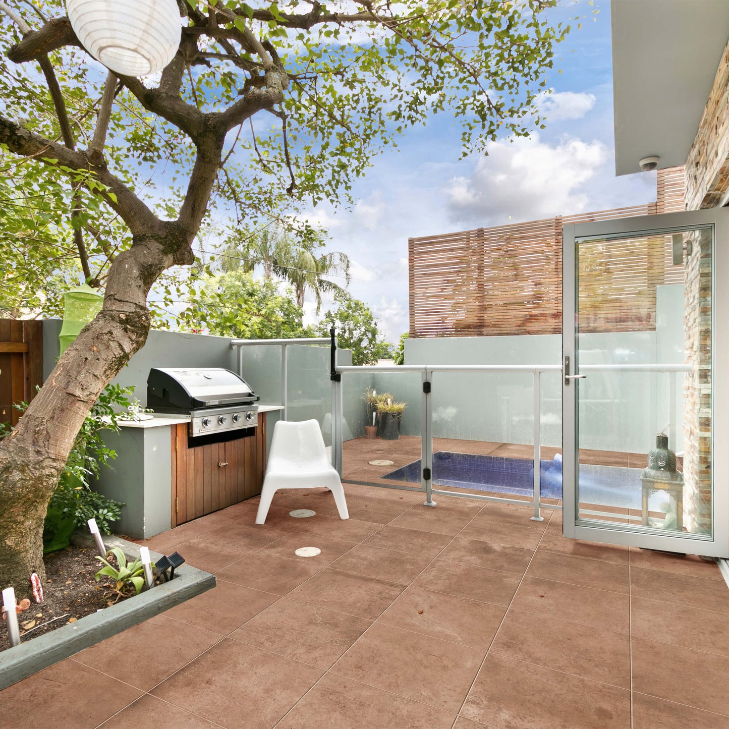 Clay Orvieto Light Terracotta 600x600mm tiles installed on a contemporary outdoor patio featuring a built-in BBQ station, mature tree, and glass pool fence.