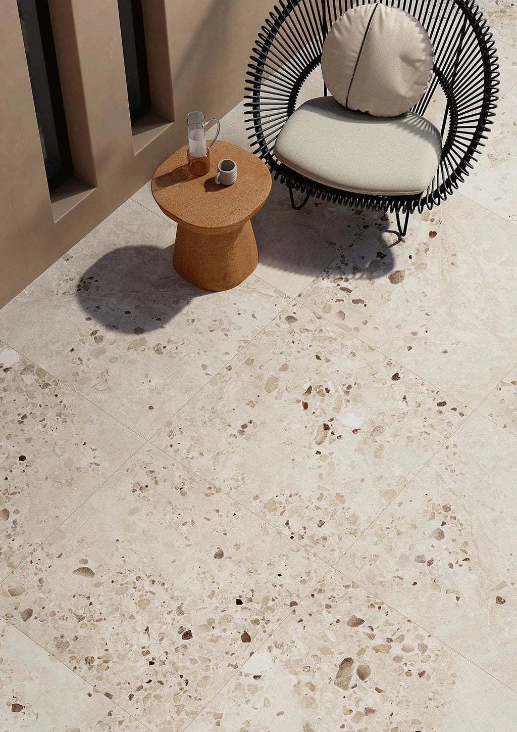 Cocci Sic. Bianco External 900x900mm terrazzo-look porcelain tiles installed on a sunlit outdoor patio with a rattan chair and timber side table.
