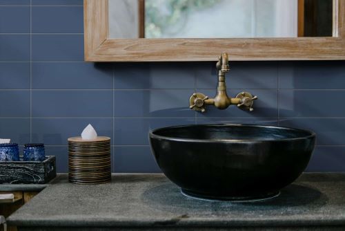 Cucina Navy Blue Gloss 100x300mm tiles installed as a bathroom vanity feature wall behind a black stone vessel sink and brass wall-mounted faucet.