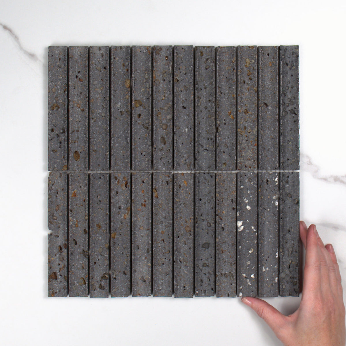 Elementa Travertine Black Concave Mosaic 23x148mm top view, hand for scale