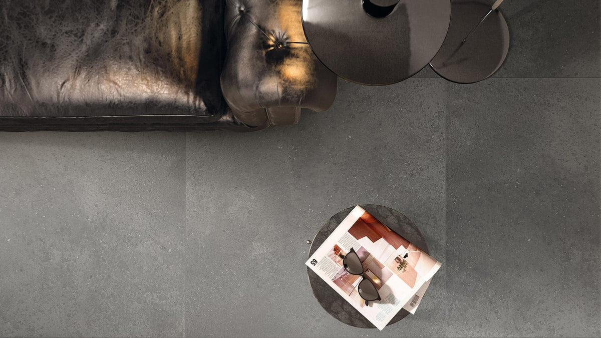 Imperial Dark Grey Matt 600x600mm porcelain floor tiles installed in a modern living room with a dark leather sofa and round metal side tables.