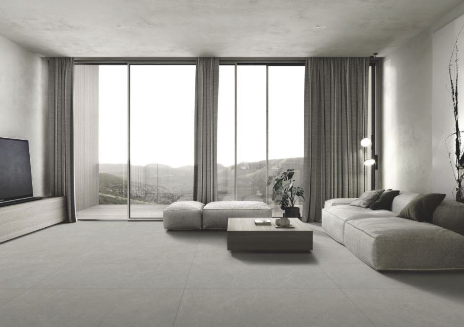 Lava Ash Amber 300x600mm large-format floor tiles in a minimalist living room with floor-to-ceiling windows, modular sofa, and mountain views.