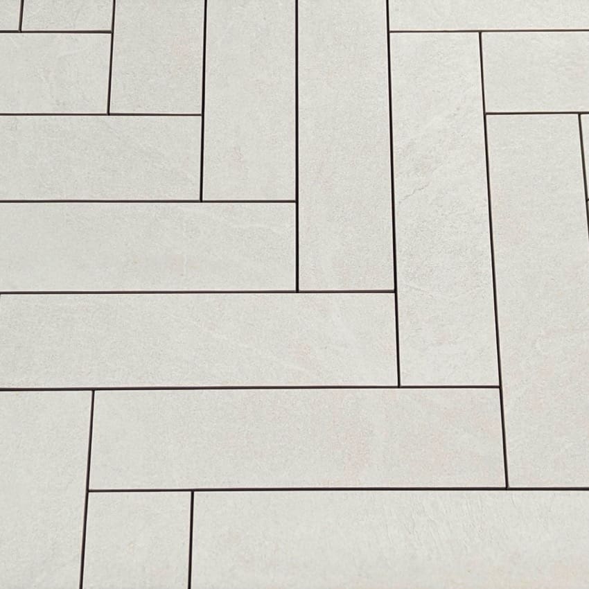 Close-up of Lava White Amber Brick/Subway 75x300mm tiles laid in a herringbone pattern with dark grout lines on a light stone-effect surface.