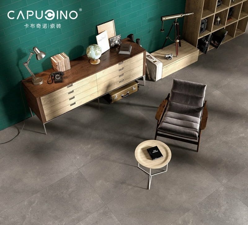 Lusso Terra Matt 300x600mm grey concrete-look floor tiles installed in a stylish living room with a recliner chair, wooden sideboard, and teal feature wall.