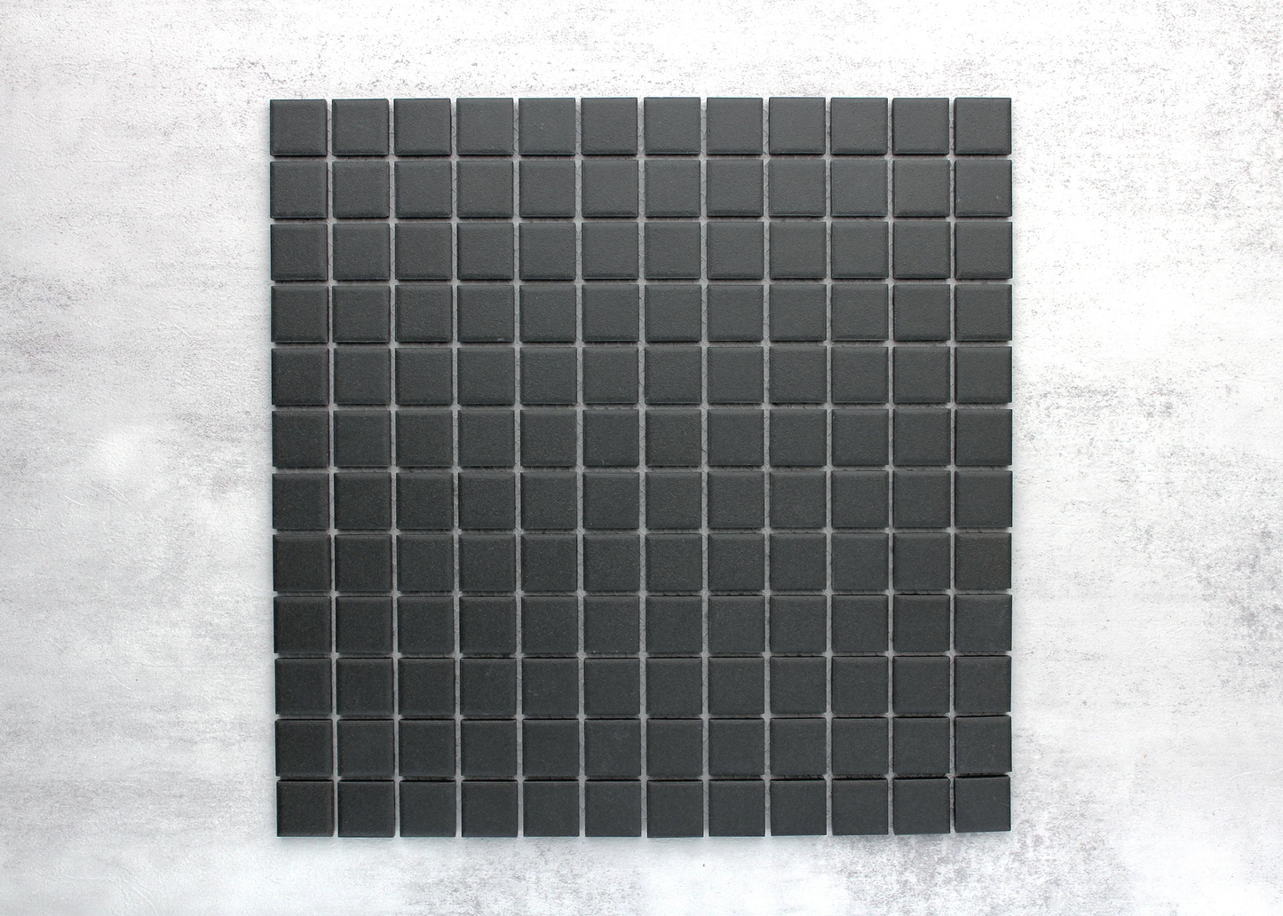 Marlowe Black Matt Mosaic 23x23mm tile sheet displaying uniformly arranged dark charcoal square mosaic tiles with a matte finish against a concrete background.