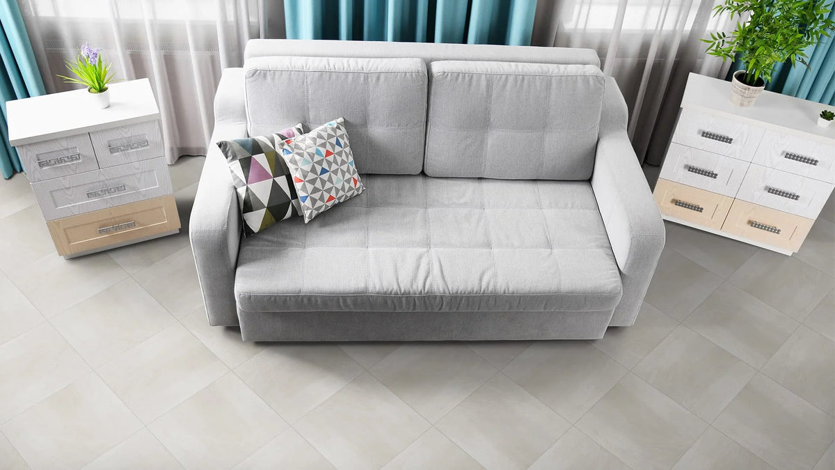 Matang Latte Gloss 300x400mm tiles laid on a bright living room floor beside a grey sofa and white drawers with teal curtains.