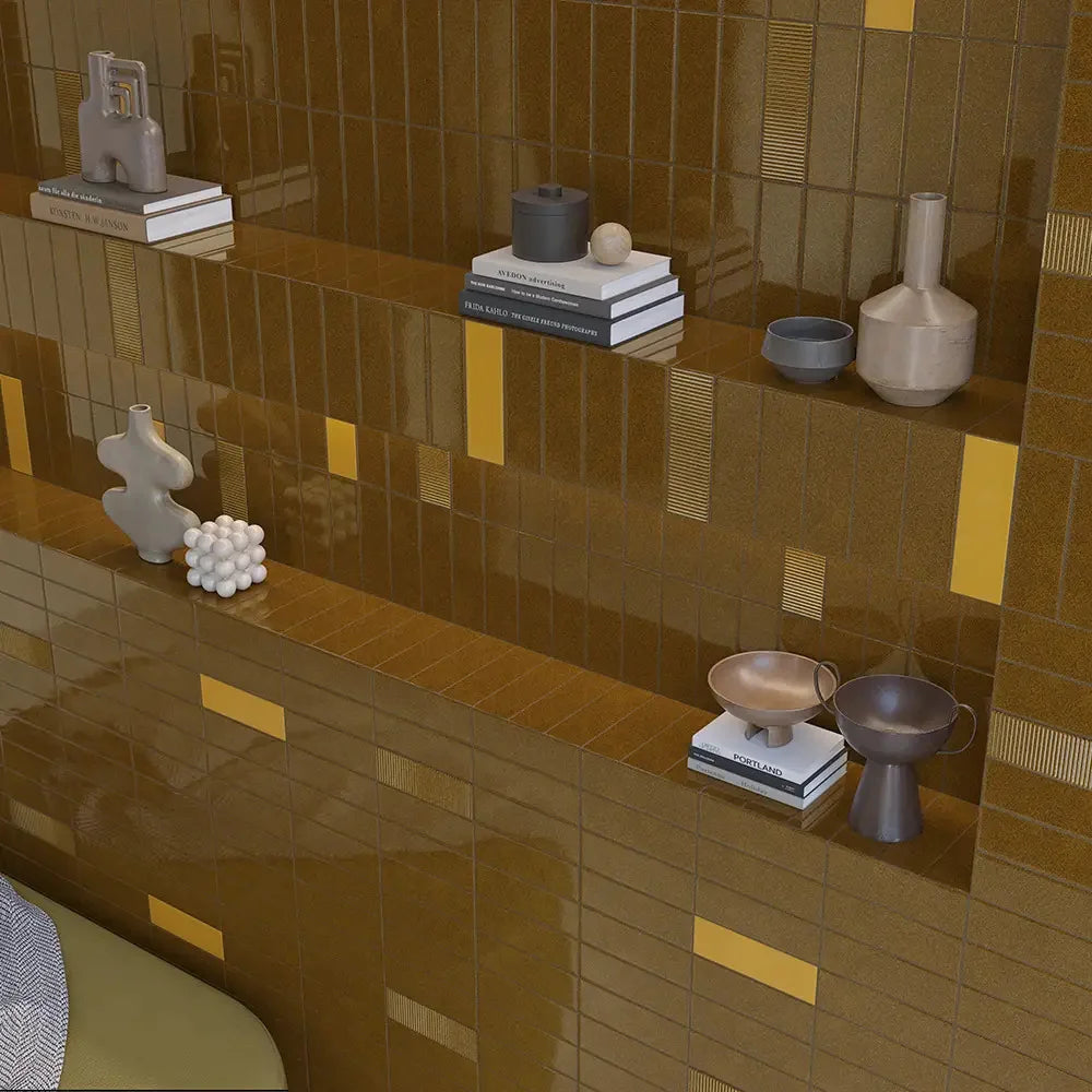 Micare Ambar Dark Gloss 50x150mm amber brick tiles forming a stepped display wall with built-in shelves styled with ceramic vases, bowls, and art books.