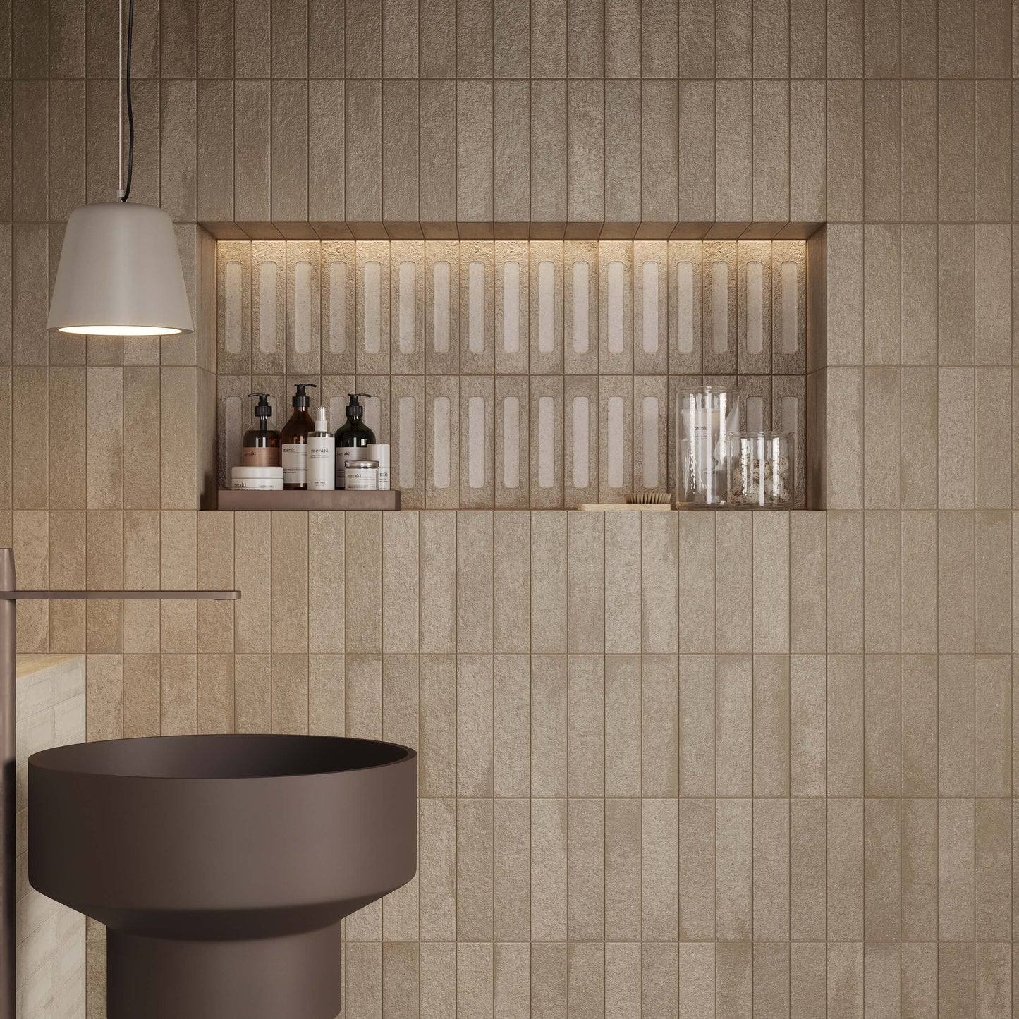 Miniature Fornace Bruno Bistro 60x240mm sand-toned textured tiles covering a bathroom wall with lit niche shelf, pedestal sink, and pendant light.