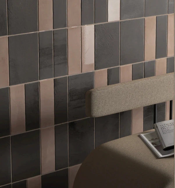 Miyako Coffee Gloss 50x150mm tiles installed as a bedroom feature wall in mixed dark charcoal and rose-copper tones behind an upholstered headboard.