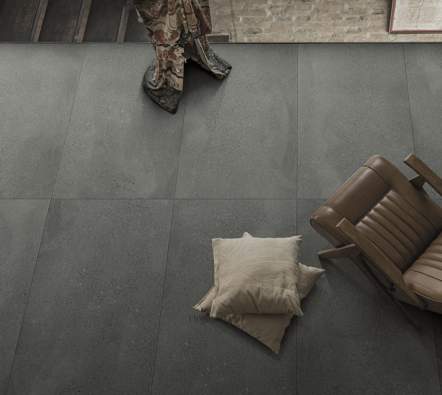 Moonstone Oyster Matte 300x600mm dark grey stone-look floor tiles installed in a contemporary living space with a leather chair and cushions.