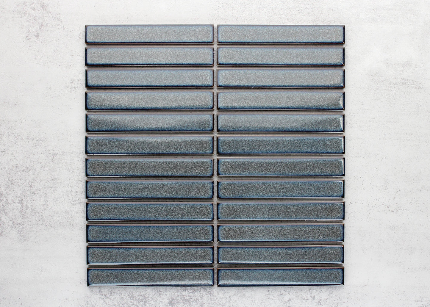 Flat lay pack shot of Mottled Grey Gloss KitKat Straight Bone Pattern 22x145mm tiles arranged in stacked rows showing glossy blue-grey finish and bevelled edges.