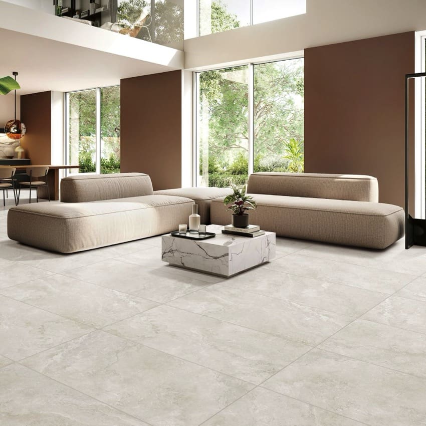 Norcia Travertine Light 300x600mm tiles installed as a spacious living room floor, complementing modular taupe sofas and a marble coffee table.