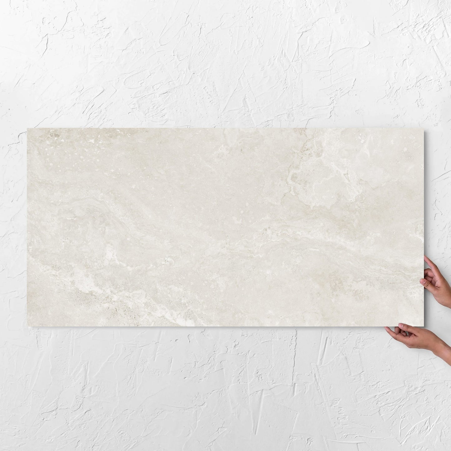 Hands holding a Norcia Travertine Light 600x1200mm tile against a white rendered wall, showing the tile surface