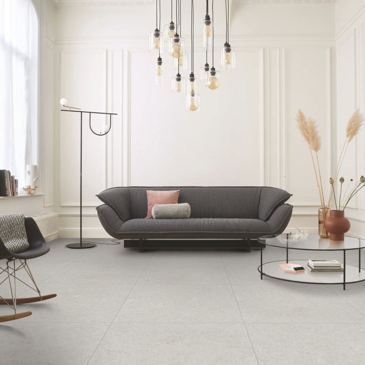 Organic Pietra Lavica Glacier 450x450mm light grey stone-effect floor tiles in a bright modern living room with dark sofa and pendant lights.