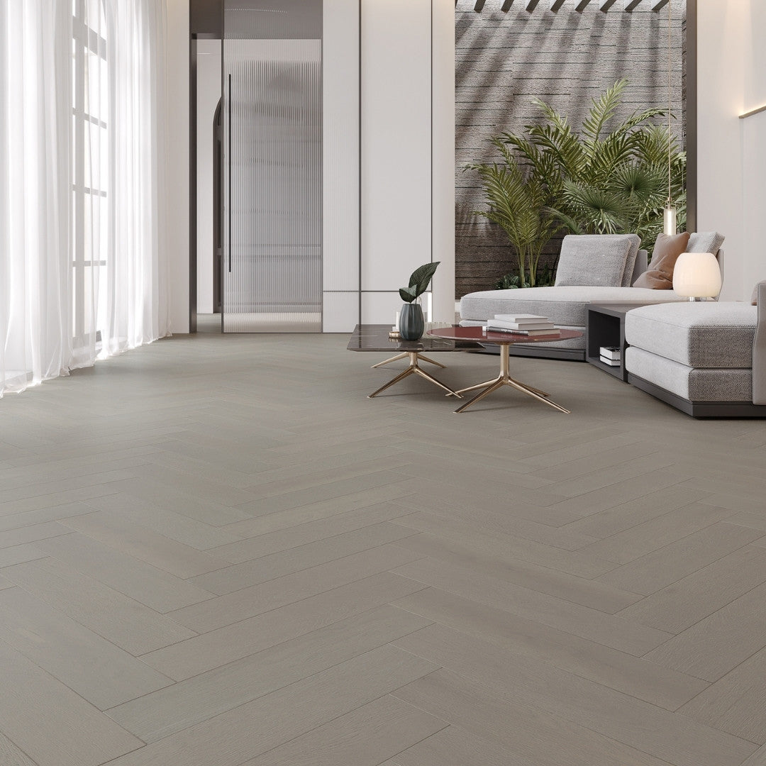 Pale Oak iDesign Herringbone Flooring 15/3mm installed in a bright open-plan living room with a sectional sofa, gold coffee tables, and tropical plants.