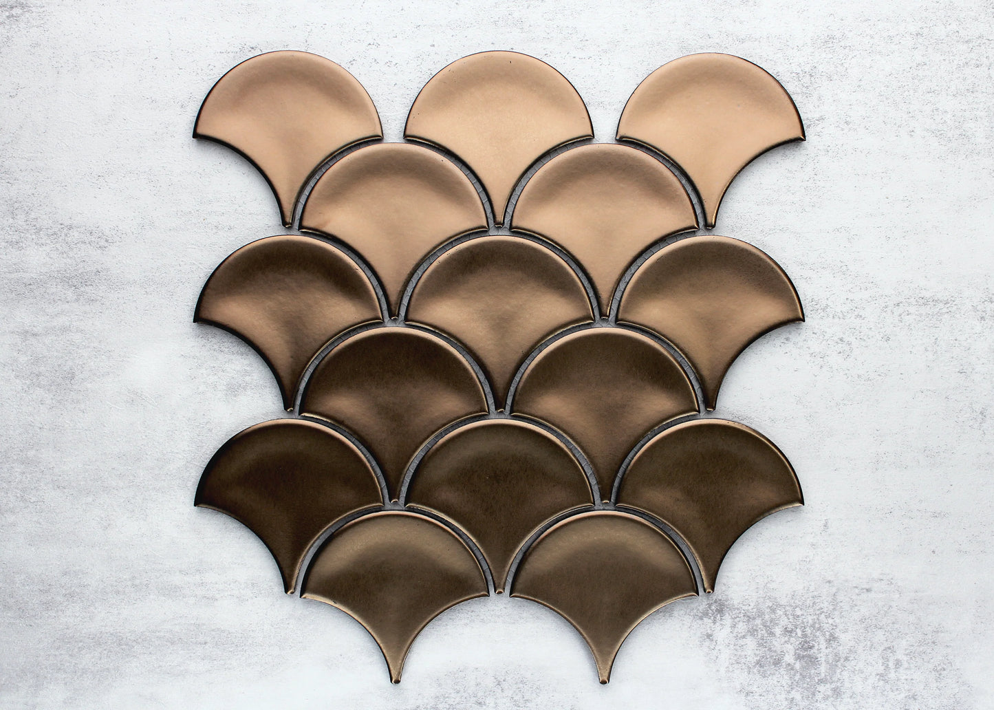 Pack shot of PGFS-0009 Bronze Metal Plated Matte Glazed Porcelain Fishscale tiles arranged in an overlapping scale pattern with an ombre effect from light tan to deep bronze.