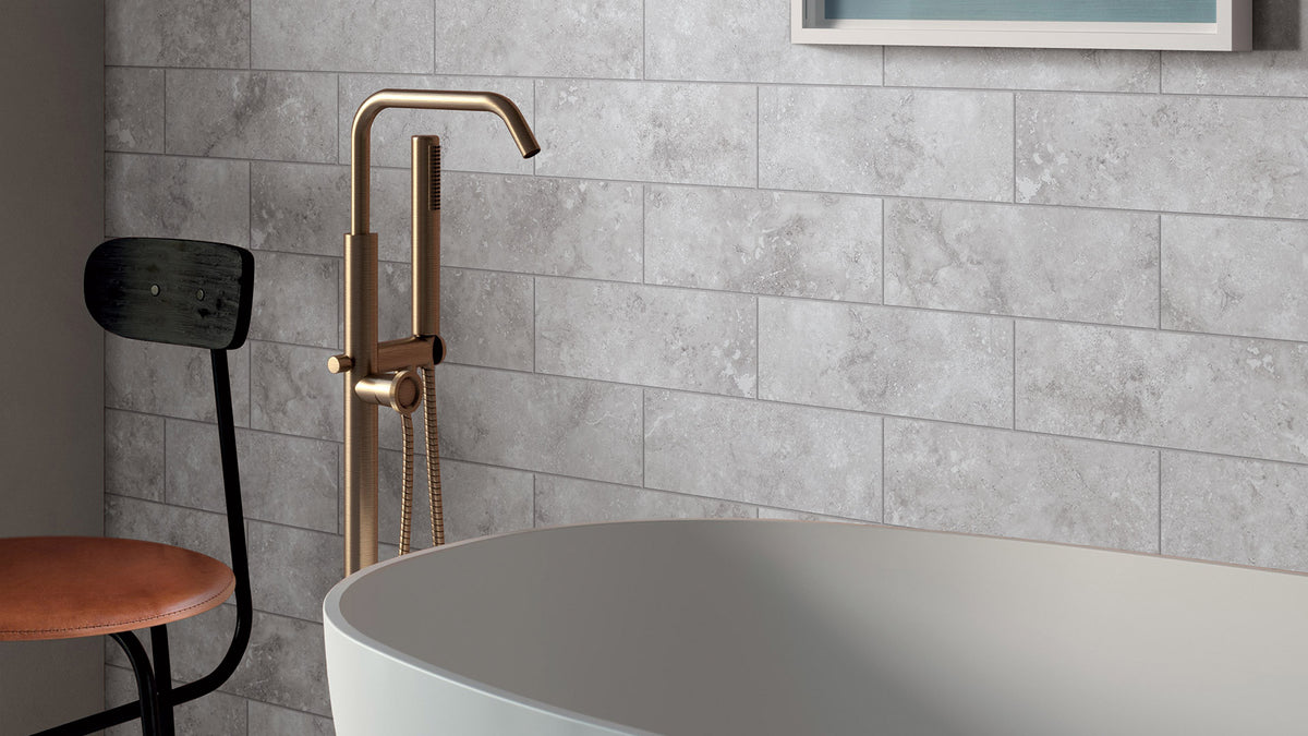Timeless Silver Structured 600x600mm grey stone-effect wall tiles installed in a luxury bathroom with a freestanding white bath and brushed brass floor-mounted tap.