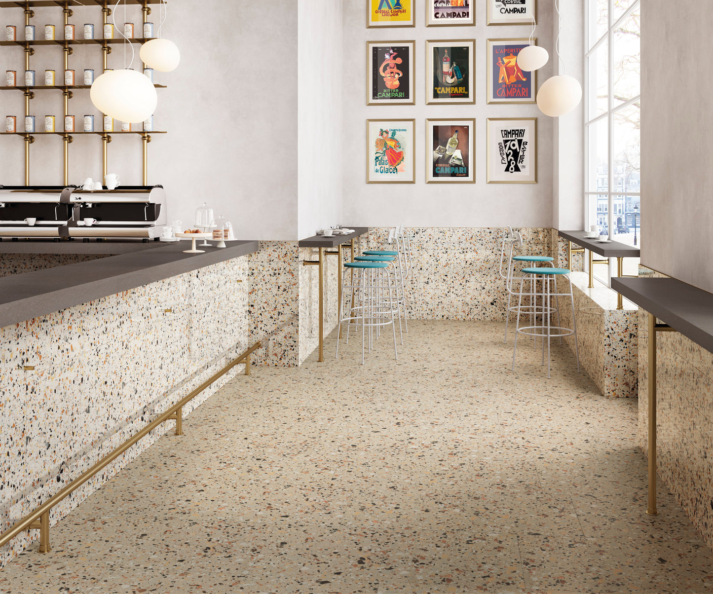 Venice Ivory 300x600mm Matt Terrazzo Tile installed across the floor and wainscoting of a stylish café bar with brass accents, globe pendant lights, and vintage Campari posters.
