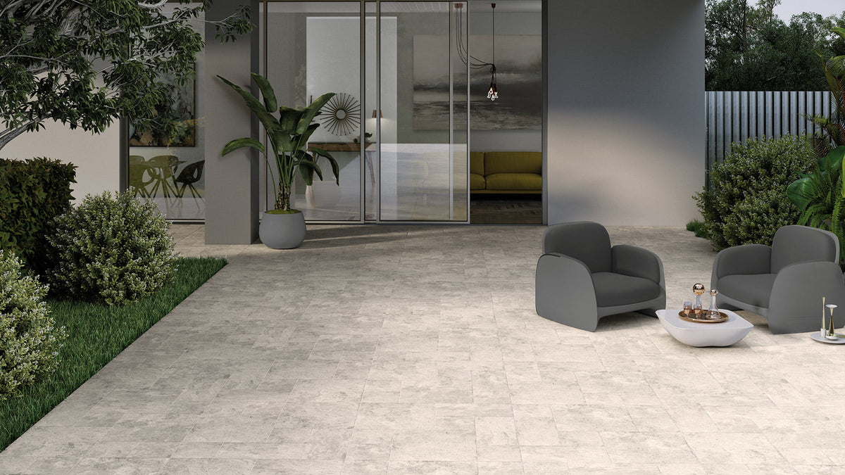 Ventor Beige Modular External tiles laid across a spacious contemporary patio with grey lounge chairs, lush garden borders, and large sliding glass doors.