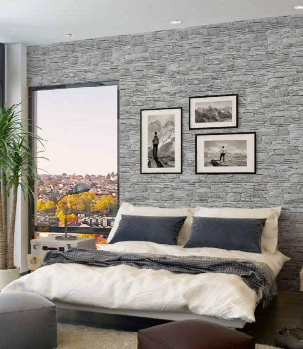 Vulcani Grigio 160x400mm grey stacked stone effect tiles covering a full bedroom feature wall behind a white bed with navy pillows and framed mountain artwork.