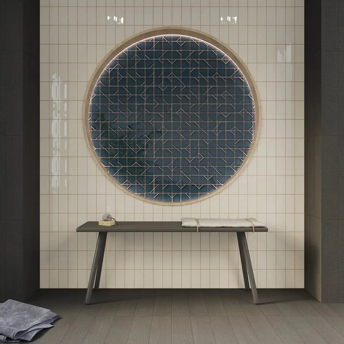 Yoko Daisy Gloss 62.5x125mm white square tiles covering a spa wall with a large circular feature panel of dark teal geometric tiles and a minimalist bench below.