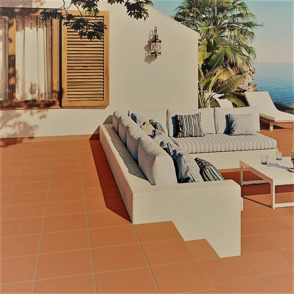 Yulara Terracotta Step Nose 300x300mm tiles laid on a sun-drenched Mediterranean outdoor terrace with white rendered built-in sofa and ocean views.