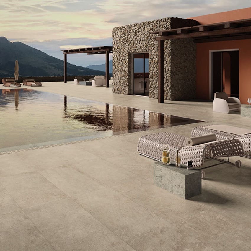 Absolute Clay 600x600mm porcelain tiles laid on a luxury outdoor pool terrace with stone-clad villa, sunloungers, and mountain views.