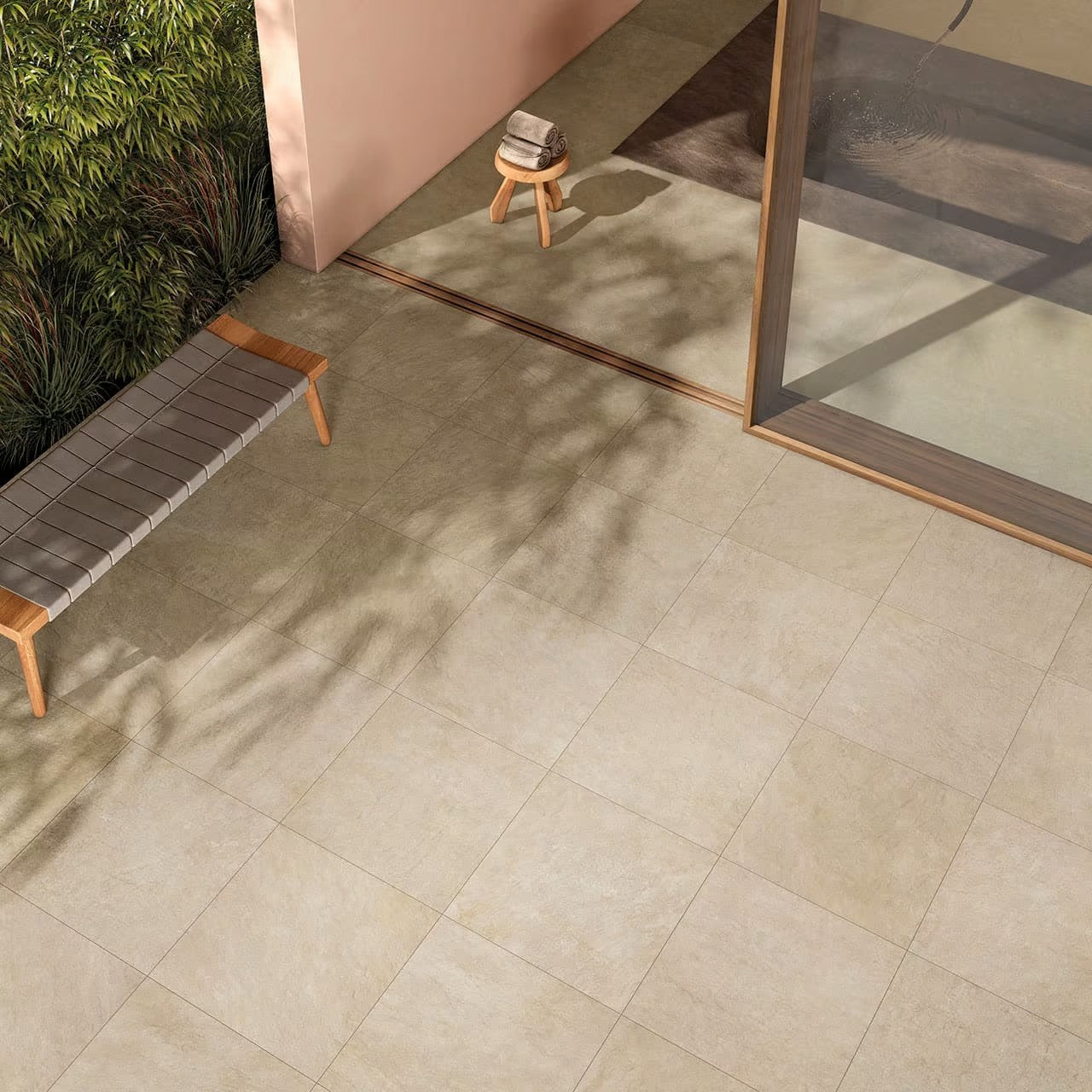 Absolute Clay 600x600mm beige stone-look porcelain tiles laid on a sunlit outdoor terrace with a timber bench and glass door.
