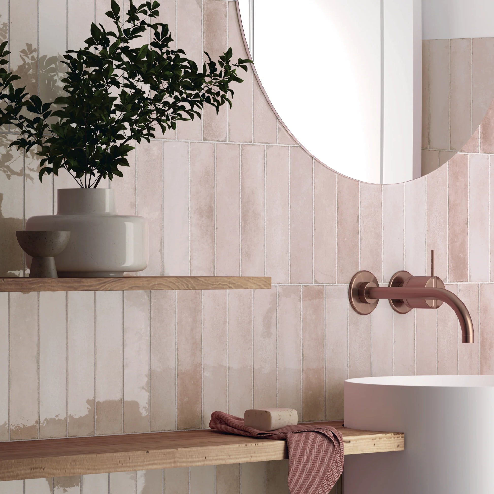 Acquarello Soft Pink Glossy 60x246mm tiles installed vertically on a bathroom feature wall with a round mirror, timber shelving, and rose gold wall-mounted tap.