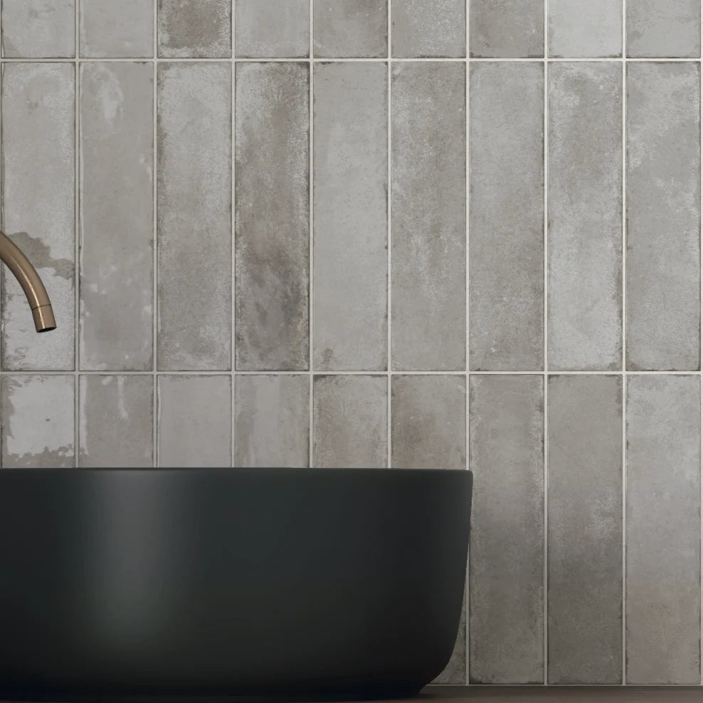 Acquarello Titanio Glossy 60x246mm tiles installed vertically on a bathroom wall behind a matte black vessel basin and brushed brass faucet.