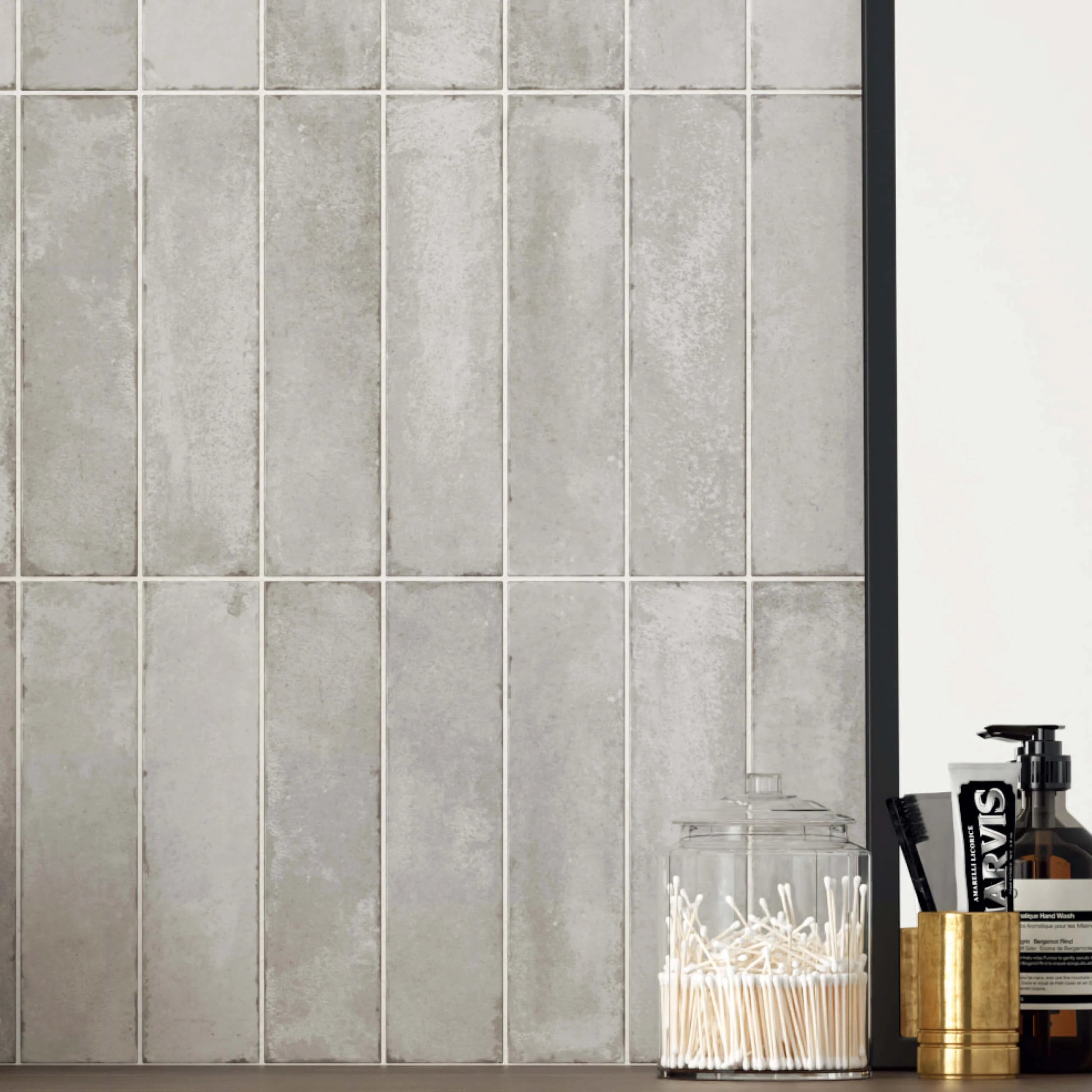 Acquarello Titanio Glossy 60x246mm tiles installed vertically on a bathroom vanity wall in mottled grey tones, styled with cotton buds, toothbrush, and Marvis toothpaste.