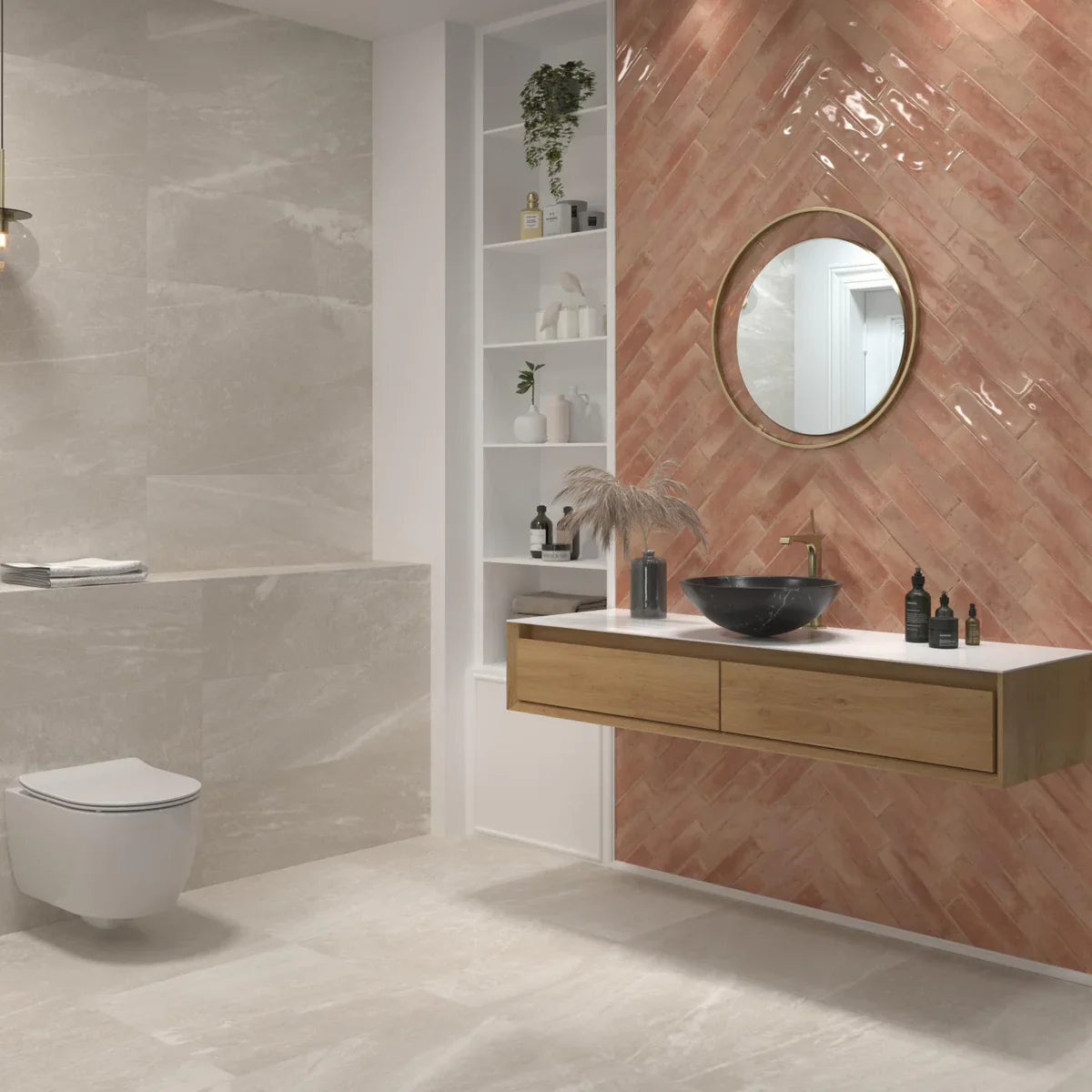 Agadir Amaranto 70x280mm glossy terracotta-pink tiles laid in a herringbone pattern on a bathroom feature wall behind a floating oak vanity with a black vessel sink and round brass mirror.