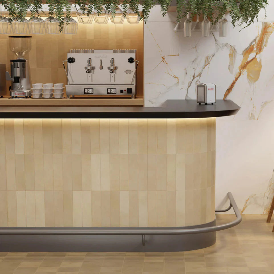 Agadir Cotto Oscuro 70x280mm tiles clad on a curved café bar counter with warm LED underlighting, marble feature wall, and hanging wine glasses above.