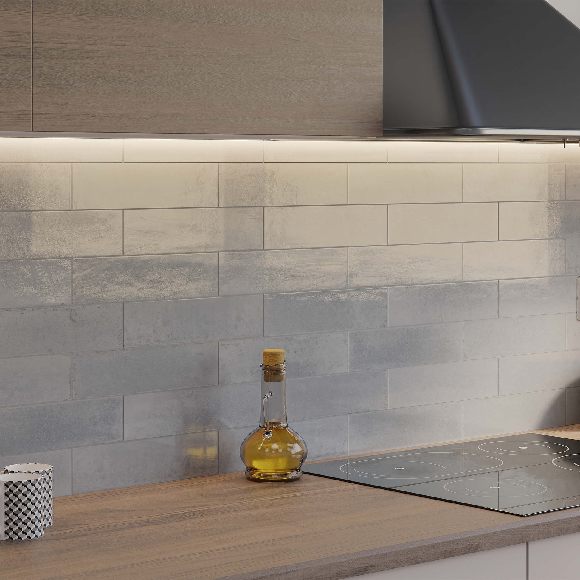 Agadir Niebla 70x280mm grey gloss subway tiles installed as a kitchen splashback behind an induction hob with wood worktop and range hood.