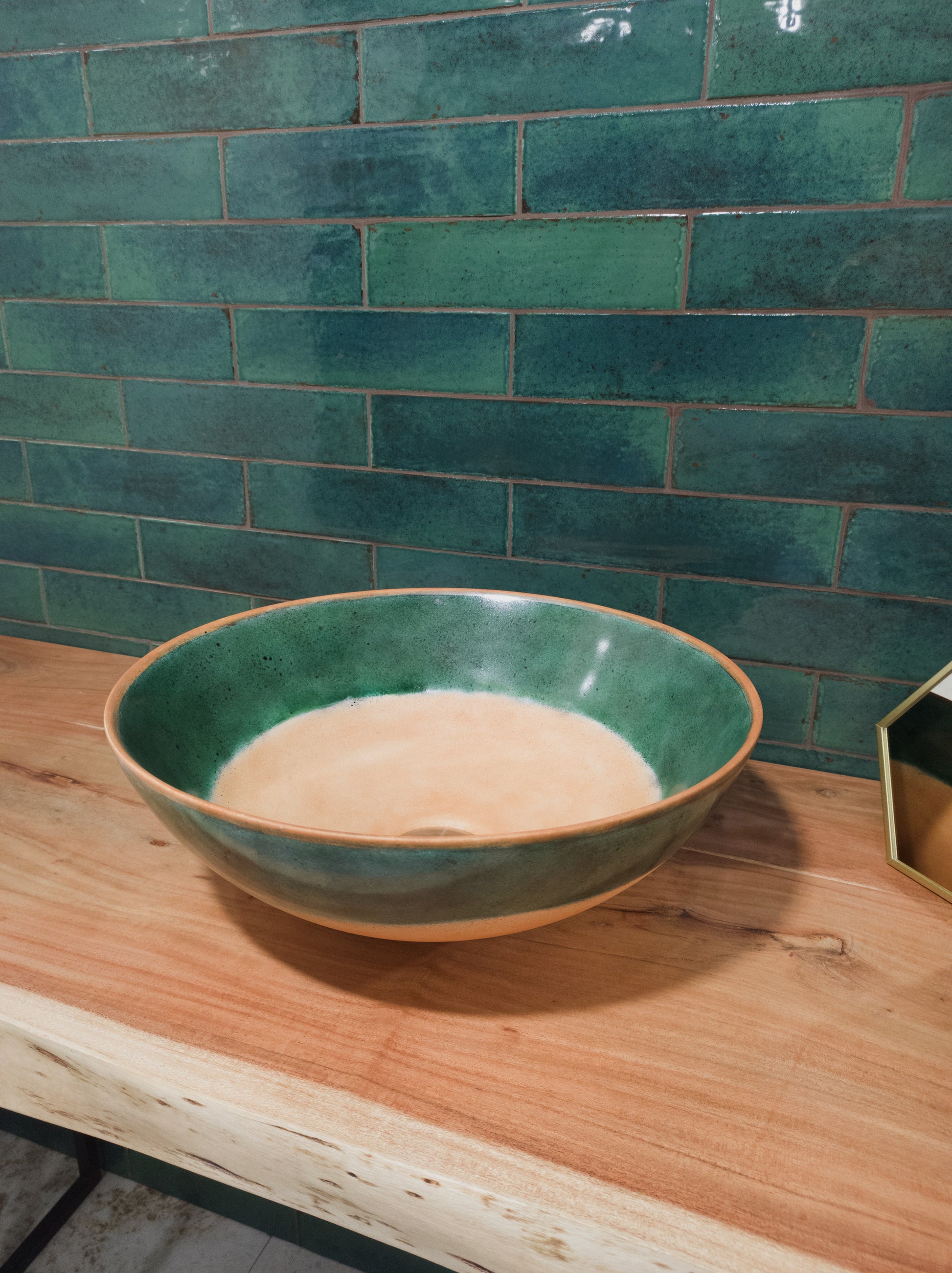 Agadir Selva 70x280mm glossy teal green subway tiles installed as a bathroom feature wall behind a ceramic vessel sink on a live-edge timber vanity.
