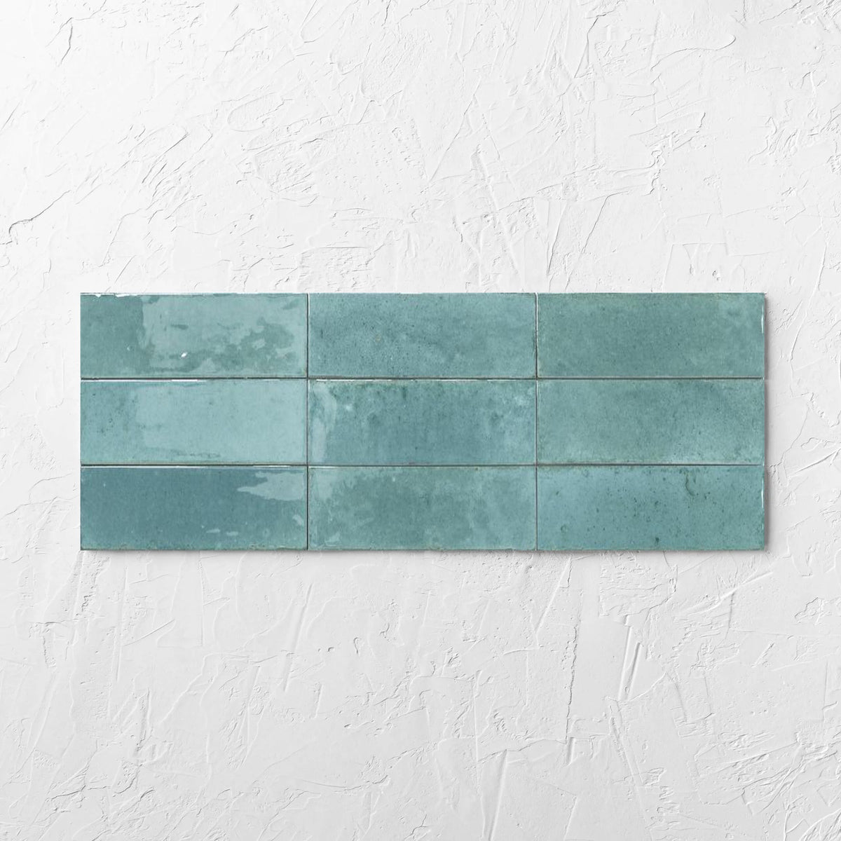 Agadir Turquesa 70x280mm tile laid flat on a white rendered wall, showing the turquoise ultra-gloss surface