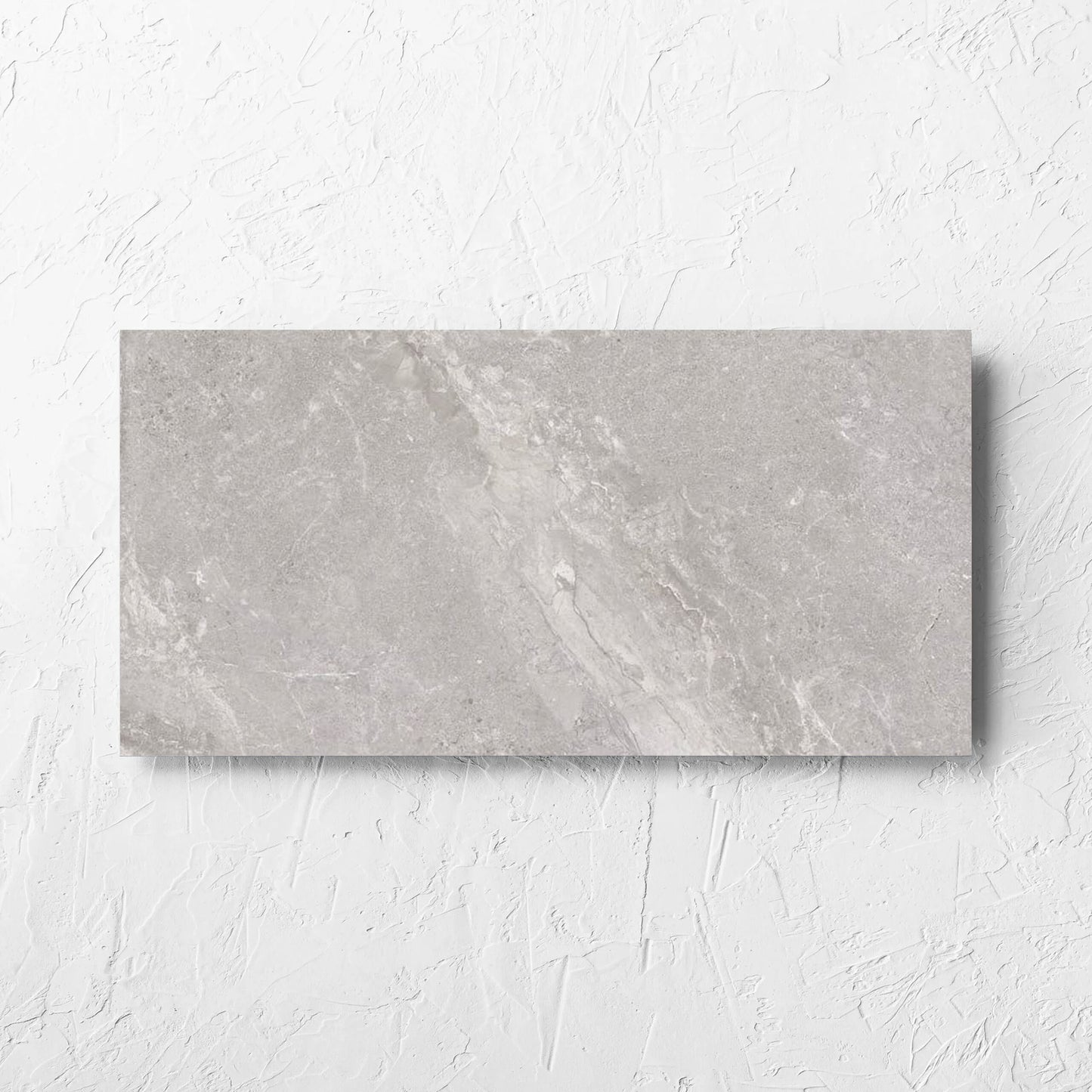 Alpen Stone Grey 300x600mm tile laid flat on a white rendered wall, showing the tile surface