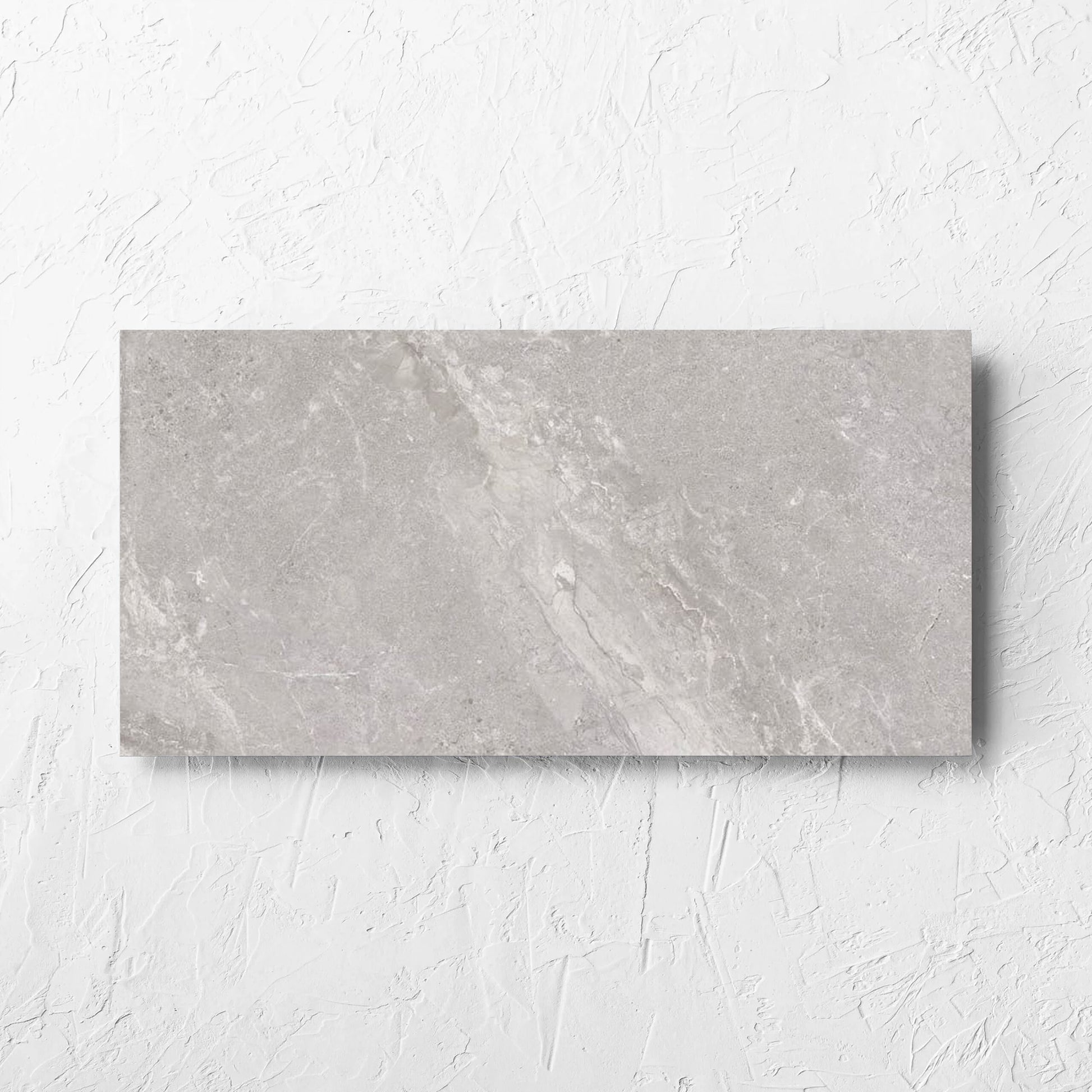 Alpen Stone Grey 300x600mm tile laid flat on a white rendered wall, showing the tile surface