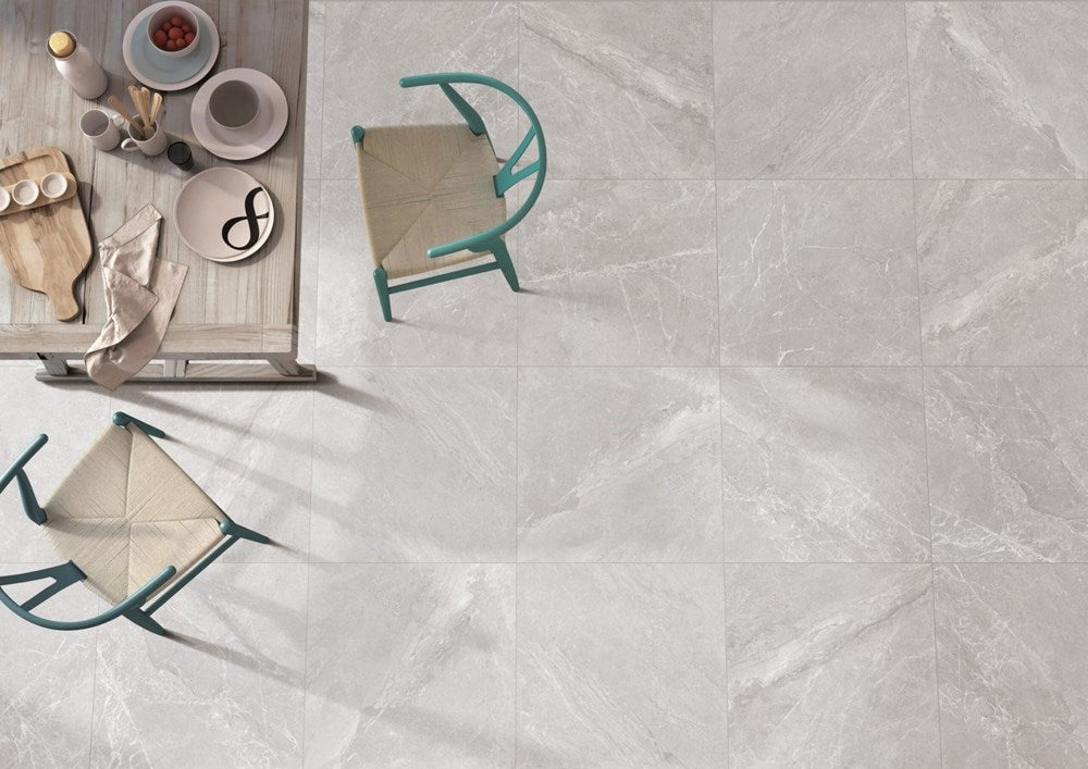 Alpen Stone Grey 600x1200mm porcelain floor tiles shown in an overhead lifestyle view with teal dining chairs and a wooden table set with ceramics.