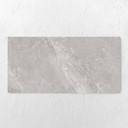 Alpen Stone Grey 600x1200mm tile laid flat on a white rendered wall, showing the tile surface